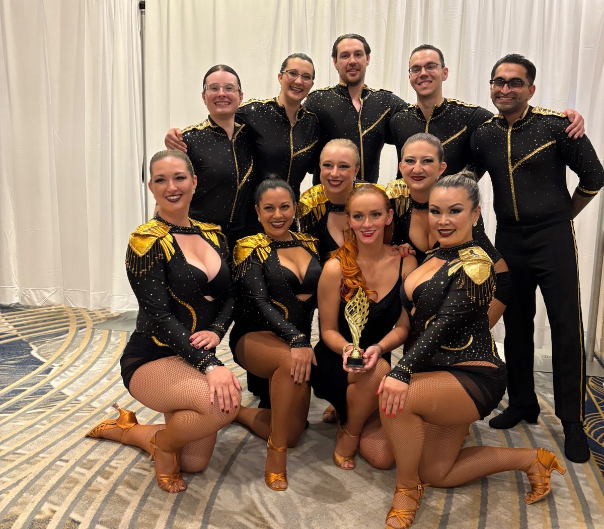 The Underdog dance team posed in two rows, a dancer in front holding a gold trophy